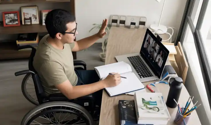 Un joven estudiante en silla de ruedas concentrado en su escritorio mientras lee unos apuntes frente a su laptop, representando la inclusión en la educación virtual.
