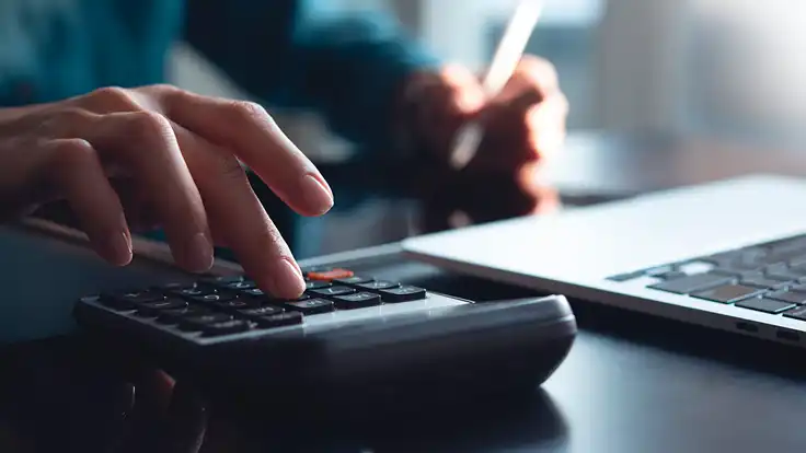 Mano de persona revisando documentos financieros con una calculadora sobre la mesa con billete peruano, representando el análisis de la tributación y la planificación dentro del sistema tributario peruano.